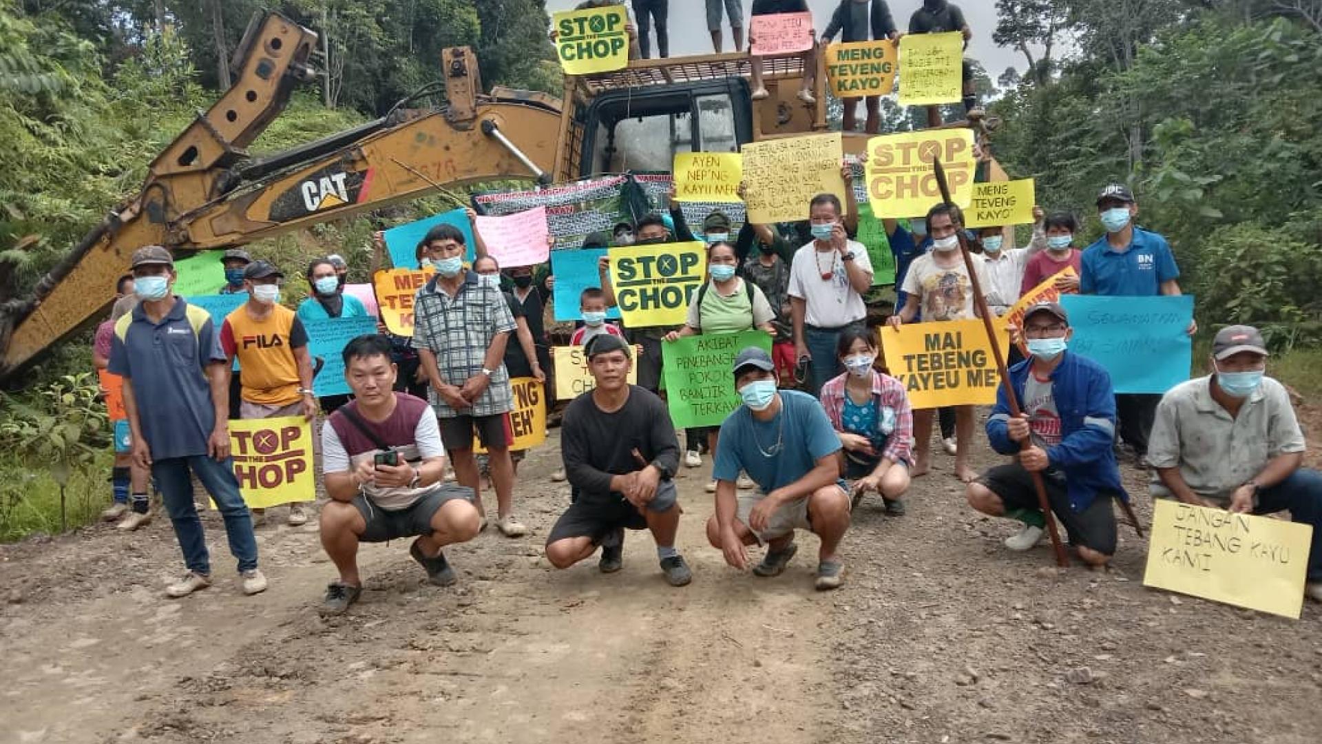 Demo by a group of Malaysian villagers standing in front of earthmoving equipment holding placards reading Stop the Chop in an attempt to protect their forest from loggers.