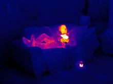 A thermal image of a man lying on a sofa at home - he is white and yellow indicating warmth, whereas his house is purple and black, indicating cold