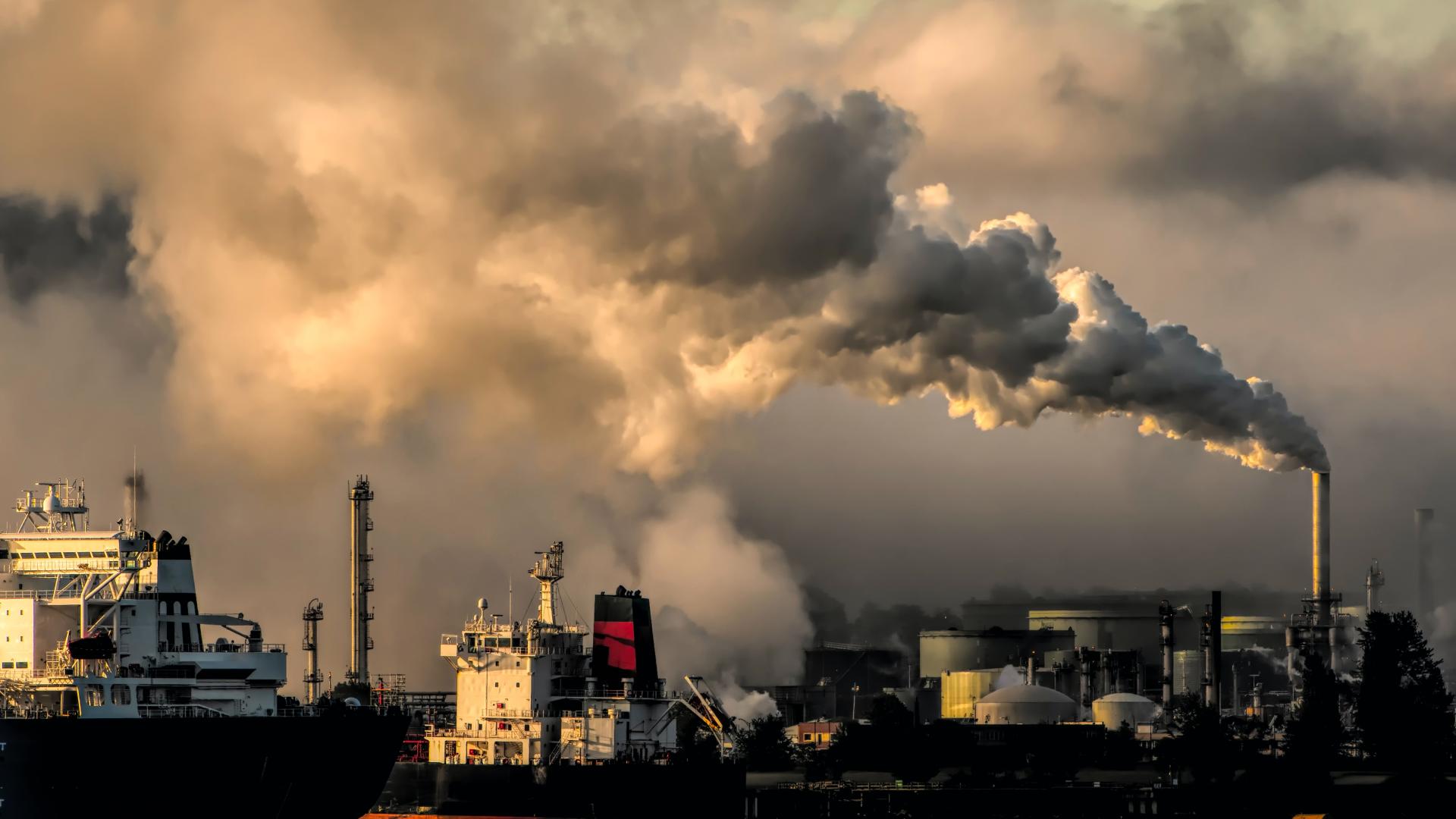 Industrial pollution, smoking chimneys, ship loading in foreground