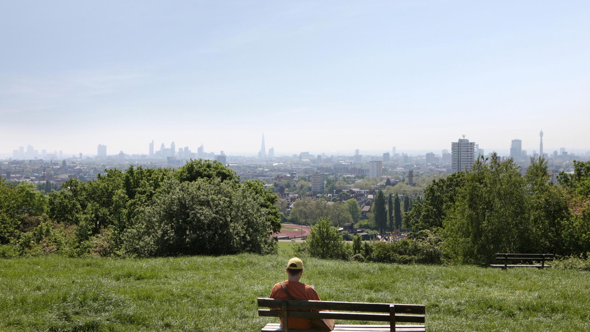 Back view of man on bench on Hampstead Heath looking at distant view of London