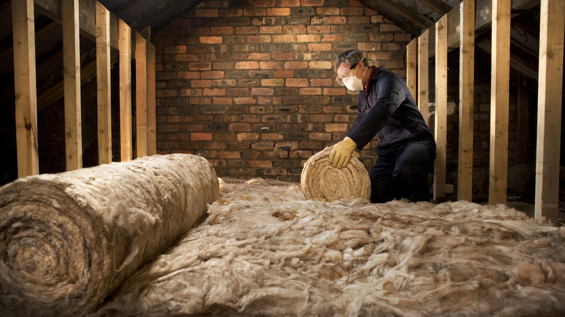 A man is rolling insulation out on the floor of a loft