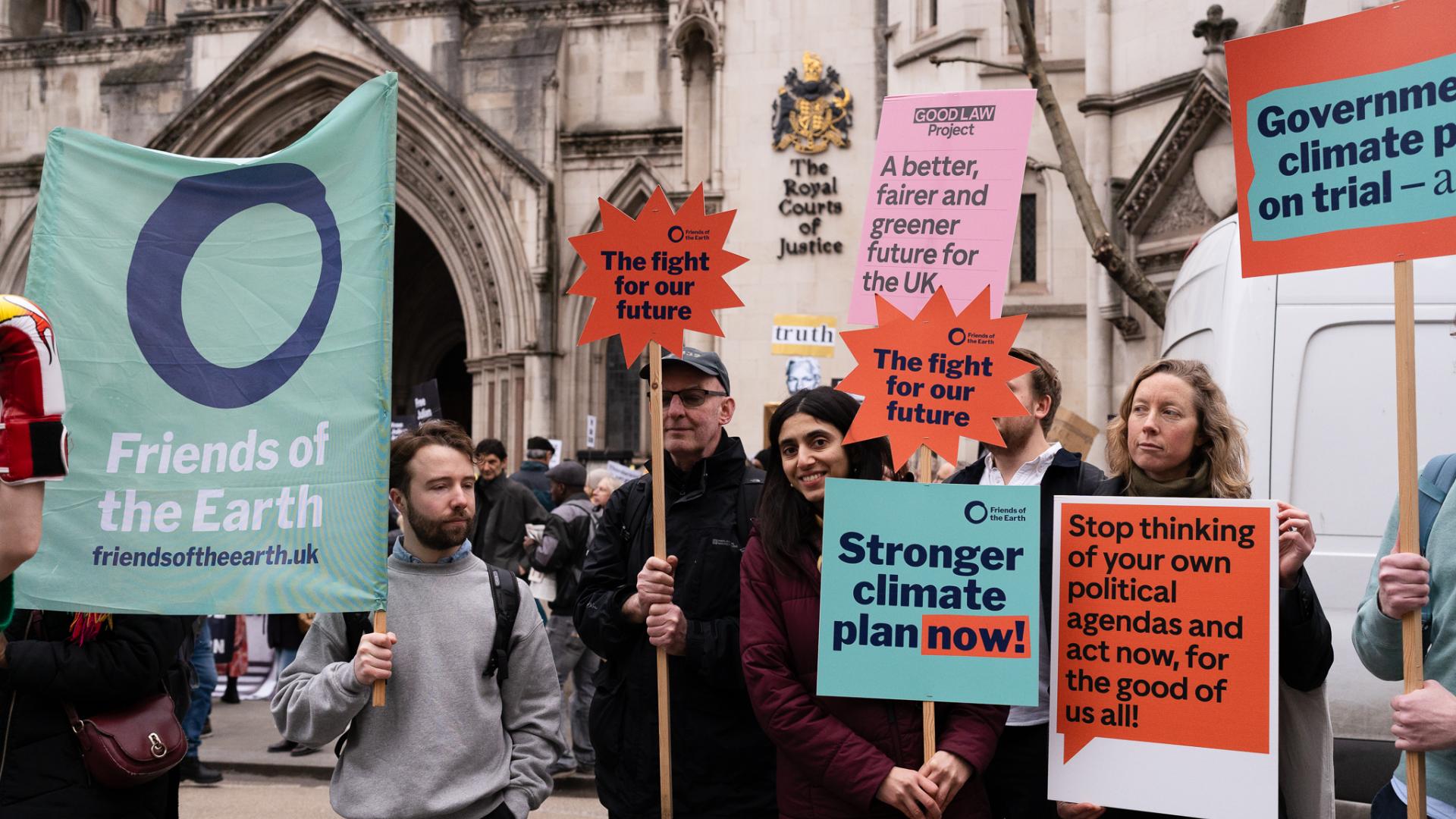 Our court case against the government's climate plan People standing outside the Royal Courts of Justice holding campaign placards and banners that say, for example, "Stronger climate plan now!"