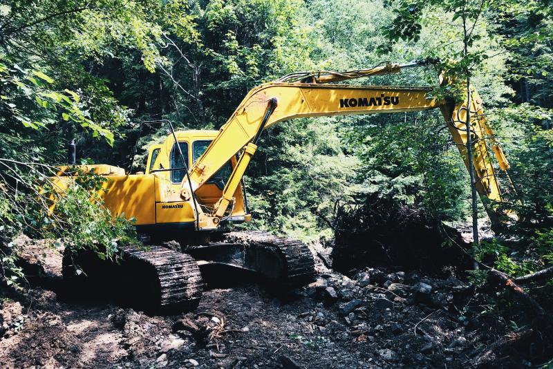 Big yellow digger clearing forest by a river