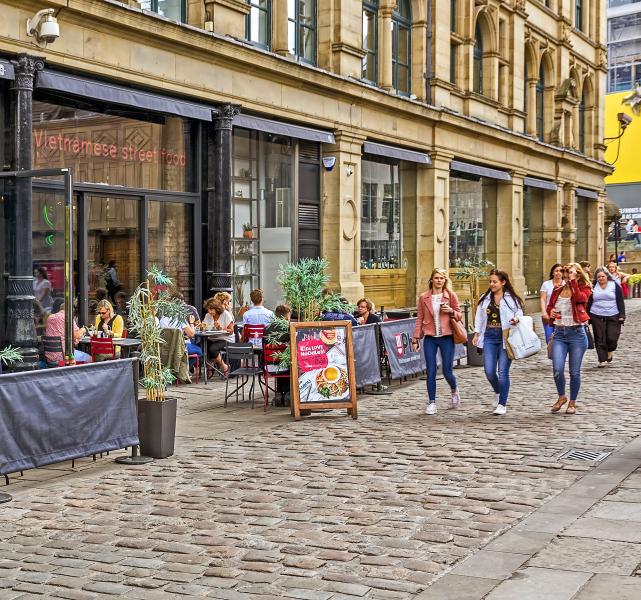Street scene in Manchester, with three women shoppers passing outdoor cafe tables with people enjoying their coffee
