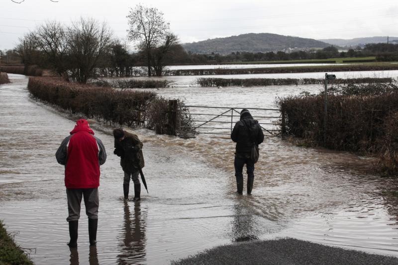 Three people wading on country road flooded by River Severn