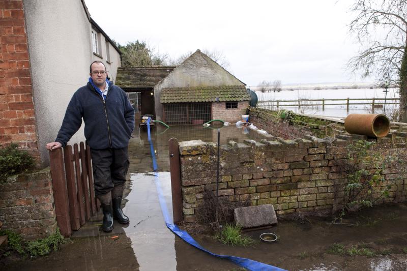 Farmer James Winslade standing in gateway outside farmhouse showing flooded garden and fields beyond