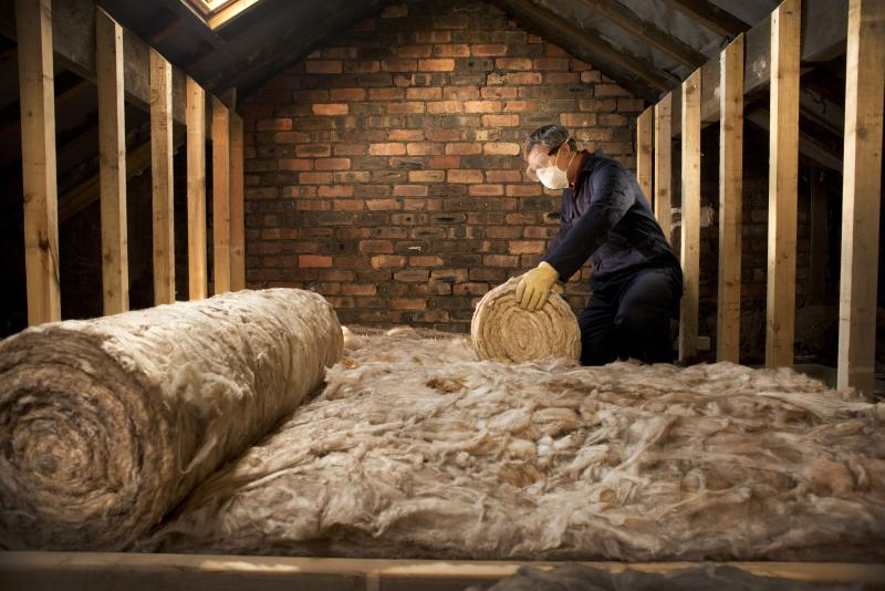 A man is rolling insulation out on the floor of a loft