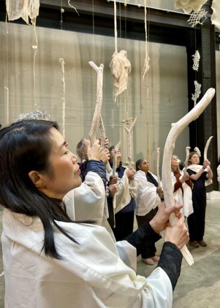 People in white shawls hold up white branches to commemorate lost forests of Borneo  at installation  at tate Modern, London
