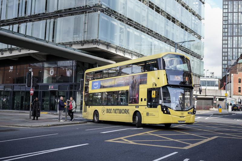 A yellow Bee Network bus driving through a junction in a city centre