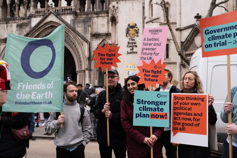 People standing outside the Royal Courts of Justice holding campaign placards and banners that say, for example, "Stronger climate plan now!"