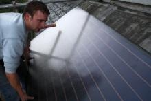 A man mounting a solar water heating panel on a roof in Hackney, UK
