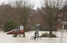 Cyclist on flooded street, submerged car in background