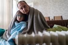 Cold father and daughter wrapped up in blankets on their sofa by a radiator