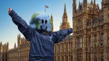 A person wearing a costume head in the shape of Earth and with their arms raised, stood in front of the Houses of Parliament 