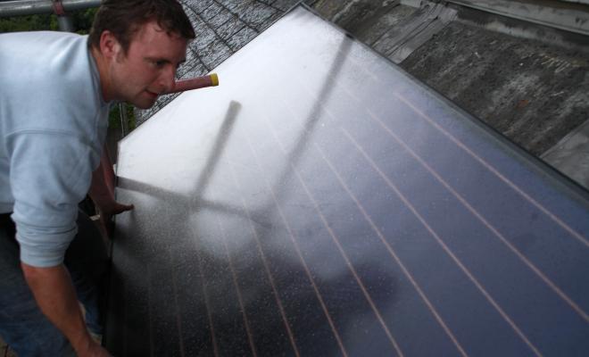 A man mounting a solar water heating panel on a roof in Hackney, UK