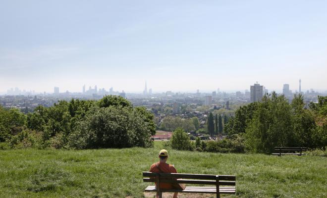 Back view of man on bench on Hampstead Heath looking at distant view of London