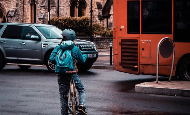 Child on bike trying to cross a busy road, traffic in background