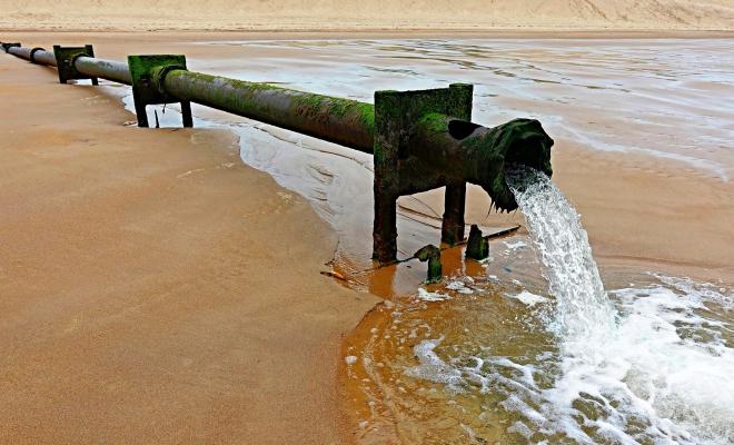 Water flowing out of sewage outfall pipe onto beach