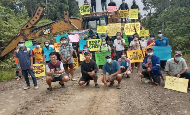 Demo by a group of Malaysian villagers standing in front of earthmoving equipment holding placards reading Stop the Chop in an attempt to protect their forest from loggers.