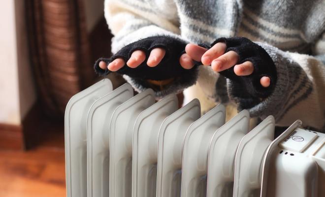 Person wearing fingerless gloves and a thick jumper, heating their hands over a radiator