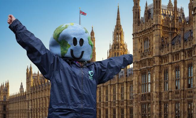A person wearing a costume head in the shape of Earth and with their arms raised, stood in front of the Houses of Parliament 
