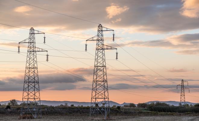 Three electricity pylons, two in the foreground, one in the background, standing in fields with a sunset sky