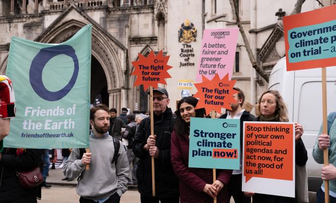 People standing outside the Royal Courts of Justice holding campaign placards and banners that say, for example, "Stronger climate plan now!"